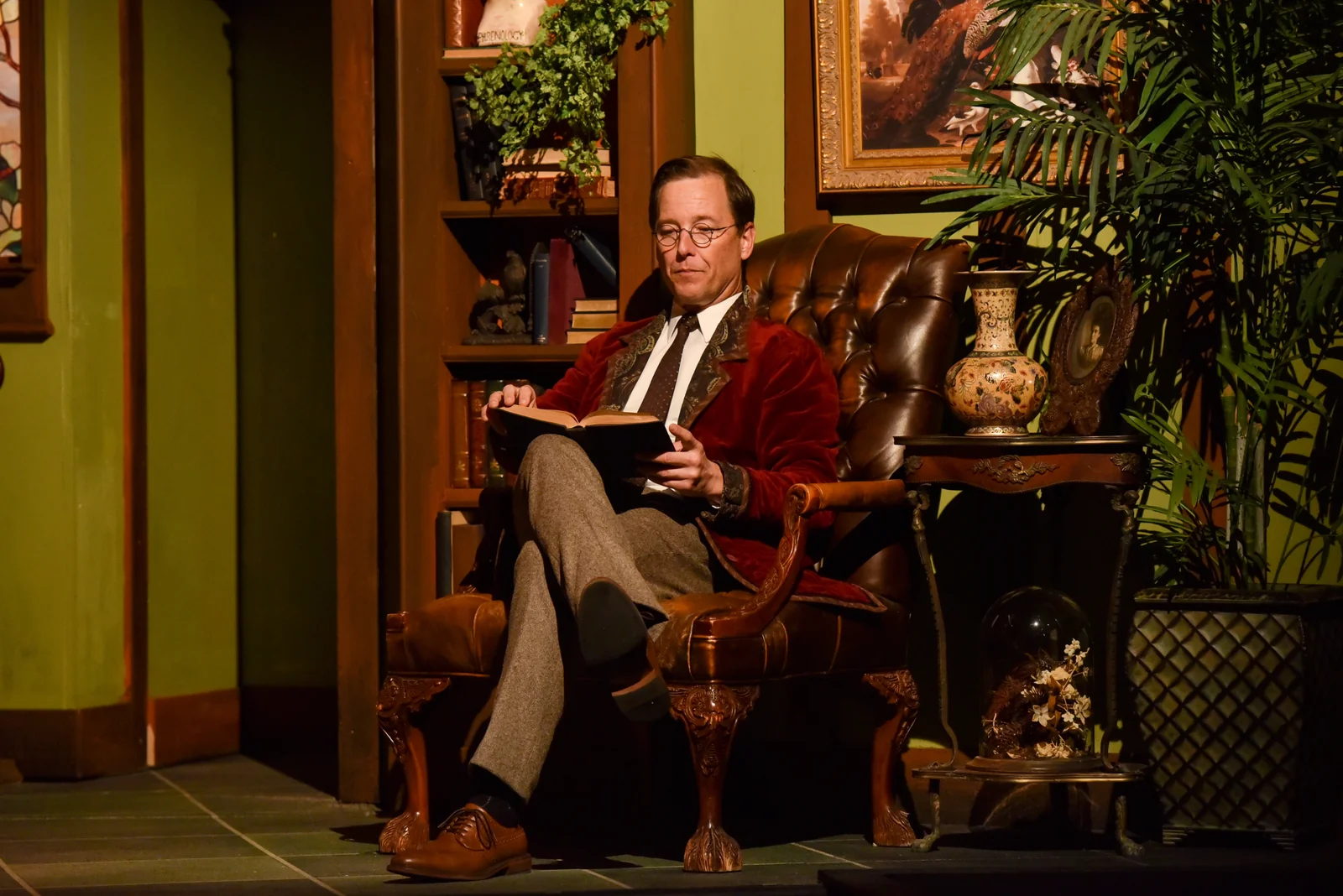 Dr. David Lowe in costume, reading a book in an armchair on stage
